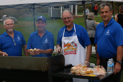 4 men helping to barbeque hotdogs